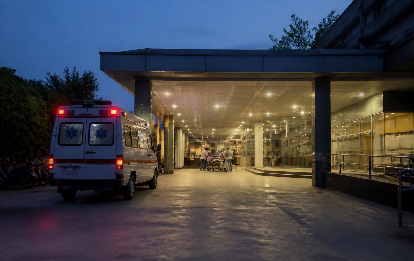 Hospital emergency entrance at dusk with an ambulance parked under the lit porch